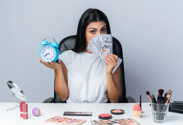 beautiful-woman-sits-table-with-makeup-tools-holding-alarm-clock-covered-face-with-cash